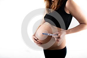 Pregnant skinny slim fit woman holding a positive pregnancy test on her belly tummy abdomen