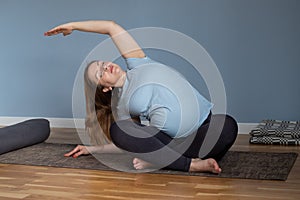 Pregnant smiling woman is sitting and doing yoga, making leans to the left side