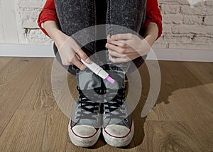 Pregnant teenager girl or young desperate woman holding positive pink pregnancy test