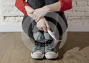 Pregnant teenager girl or young desperate woman holding positive pink pregnancy test