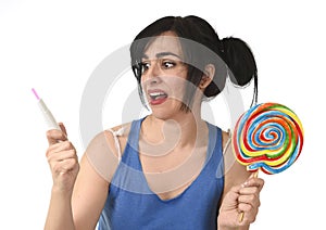 Pregnant teenager holding big lollipop while checking positive pink result on pregnancy test