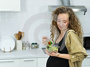 pregnant vegetarian woman smile, happy, stand, eat vegetable, look at vegetable salad cup in kitchen with copy space. beautiful