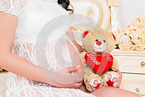 Pregnant in a white lace dress with teddy bear