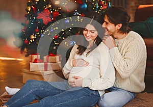 Pregnant wife and her husband sitting by Christmas tree