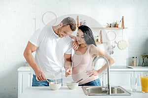 Pregnant wife and husband making cereals with milk in kitchen