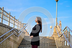 Pregnant woman against the blue sky. Portrait of a young pregnant woman against a clear blue sky, urban pregnancy, beautiful and