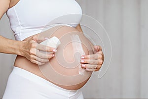 Pregnant woman aplying cream at her belly for prevention of stretch marks on the skin photo