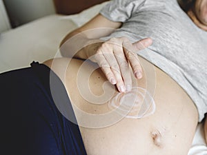 Pregnant woman applying body cream on baby bump