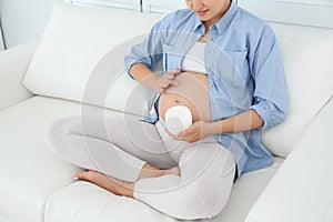 Pregnant woman applying body cream on belly
