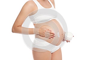 Pregnant woman applying body cream on belly against white background