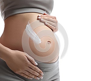 Pregnant woman applying cosmetic product on belly against white background, closeup