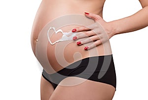 Pregnant woman applying cream on her belly, skin care, heart