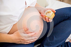 Pregnant woman applying creme on her belly to prevent strech marks