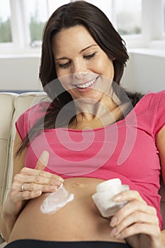 Pregnant Woman Applying Moisturiser To Belly At Home photo