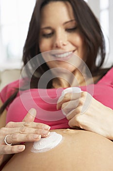 Pregnant Woman Applying Moisturiser To Belly At Home