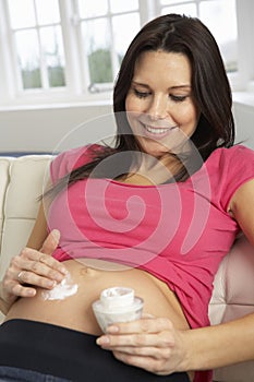 Pregnant Woman Applying Moisturiser To Belly At Home photo