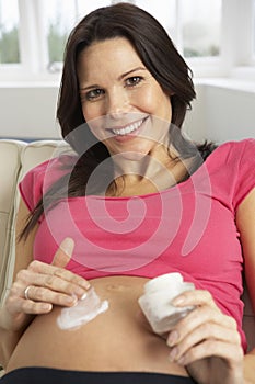 Pregnant Woman Applying Moisturiser To Belly At Home