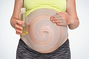 Pregnant woman is applying moisturizing body oil on belly