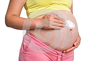 Pregnant woman is applying moisturizing cream on her belly