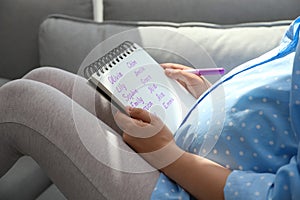 Pregnant woman with baby names list sitting on sofa