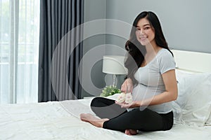 Pregnant woman with baby socks or shoes on bed