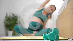 A pregnant woman on background. Focus on foreground at dumbbells. Sport concept.