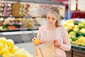 Pregnant woman with bag buying oranges at grocery