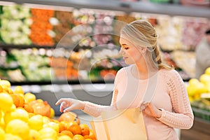 Pregnant woman with bag buying oranges at grocery