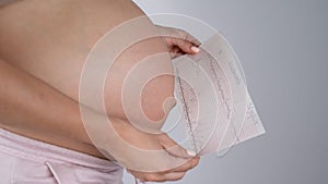 Pregnant woman with bare belly holding Cardiotocography results.