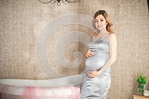 Pregnant woman in the bathroom close-up. Pregnant near the bath in a gray peignoir and copy space