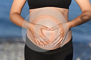 Pregnant woman beach - hands in heart shape on belly