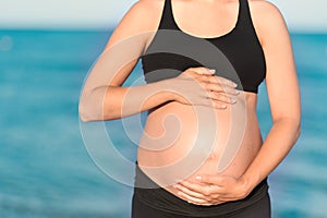 Pregnant woman beach - hands in heart shape on belly