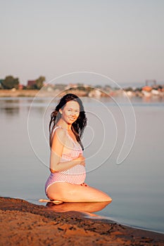 pregnant woman on the beach, Peaceful, asian pregnant woman in a pink swimsuit is sitting on her knees on the beach with