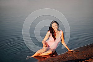 pregnant woman on the beach, Peaceful, relaxed pregnant woman in a pink swimsuit sitting on the sandy beach of the sea
