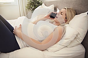 Pregnant woman on the bed at home having contractions holding cellphone