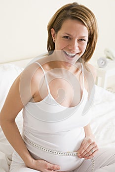 Pregnant woman in bedroom measuring belly