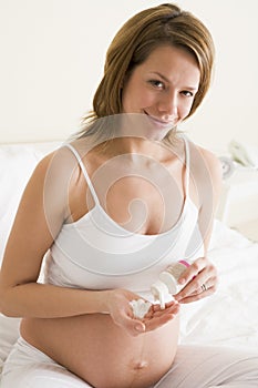 Pregnant woman in bedroom with medicine smiling