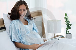 Pregnant woman in bedroom reading fairy tales to the baby in the womb in the morning