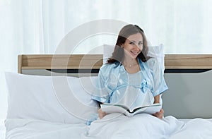 Pregnant woman in bedroom reading fairy tales to the baby in the womb in the morning