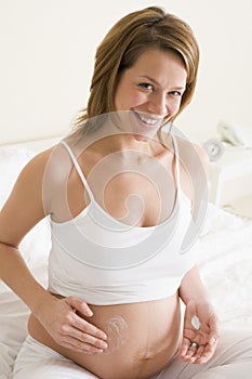 Pregnant woman in bedroom rubbing cream