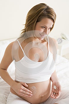 Pregnant woman in bedroom rubbing cream on belly