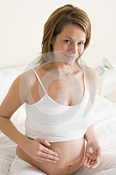 Pregnant woman in bedroom rubbing cream on belly