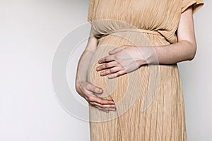 Pregnant woman in beige dress touching belly, preparing go to maternity hospital for childbirth. Pregnancy, maternity