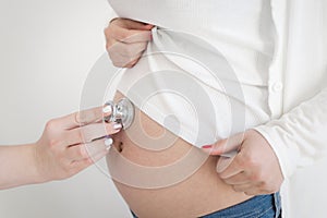 Pregnant woman being examine by a doctor with a stethoscope.