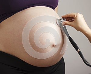 Pregnant woman being examined by doctor on gray studio background, stethoscope on belly,health care concept