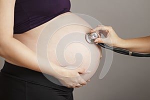 Pregnant woman being examined by doctor on gray studio background, stethoscope on belly,health care concept