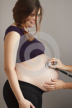 Pregnant woman being examined by doctor on gray studio background, stethoscope on belly,health care concept