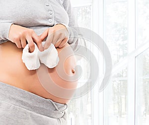 A pregnant woman with a belly holding baby shoes