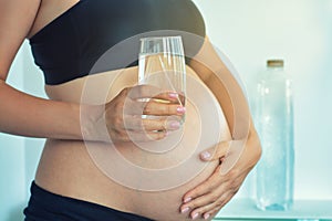 Pregnant woman belly holding a glass of water suggesting importance to hydrate during pregnancy