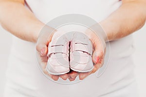 Pregnant woman belly holding pink baby booties